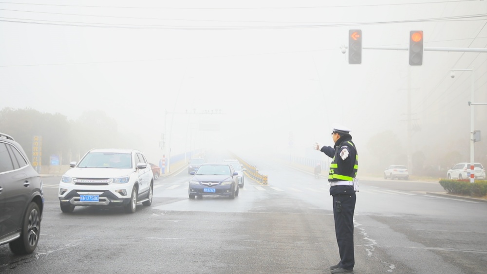 图为执勤民警正在大雾中指挥过往车辆有序通行.jpg